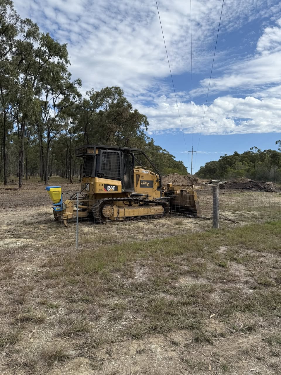 CAT D3K2 dozer with LEH cab decal on a fenced clearing, eucalypt forest behind
