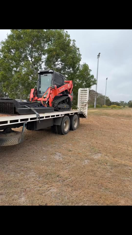 Kubota track loader with slasher attachment loaded on a flatbed truck near a sports field